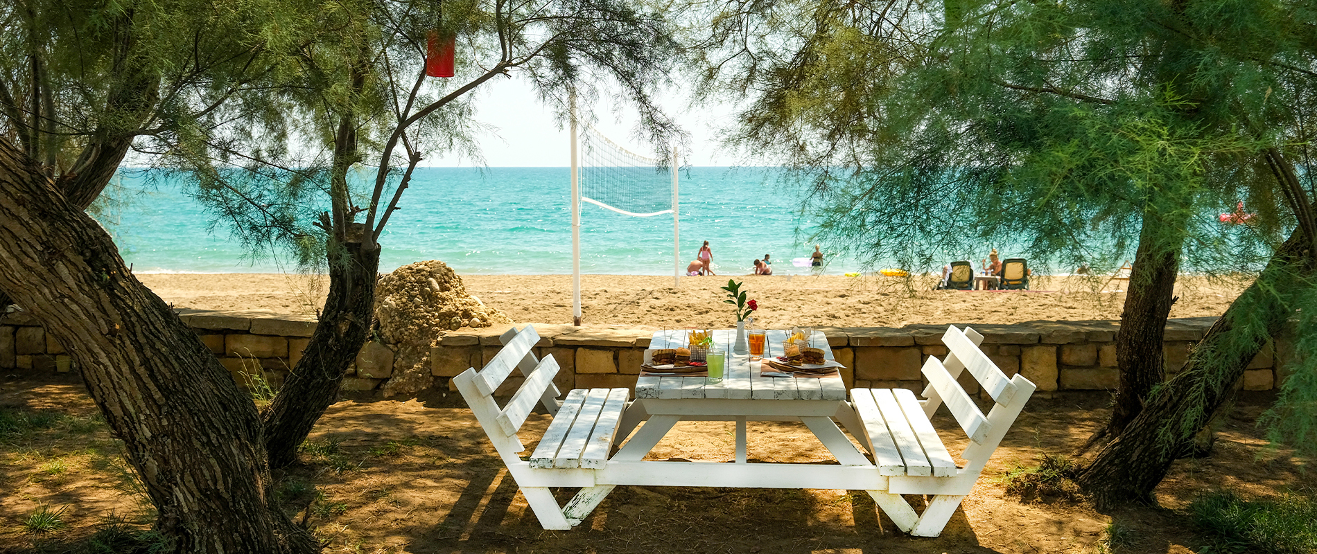 Einladend gedeckter Tisch im Schatten – genießen mit Blick auf das funkelnde Meer Gedeckter Tisch mit Bank und Stühlen im Schatten mit Blick aufs Meer