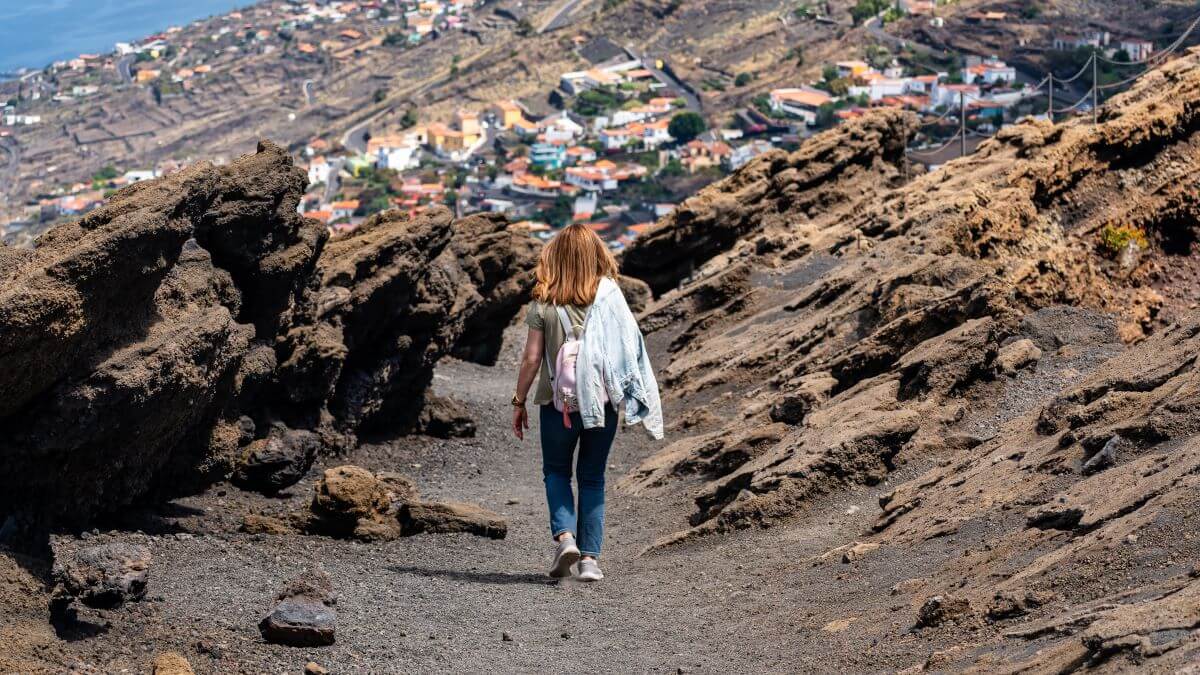 Touristin auf ihrem Rücken, die entlang des Kraterrands des Teneguia Vulkans geht
