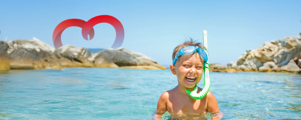 Ein fröhliches Kind steht im Meer, trägt eine Tauchmaske und lacht vergnügt Kind mit Tauchmaske lacht im Meer