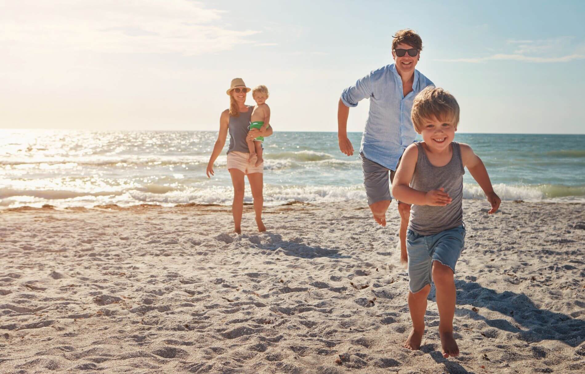 Ein fröhliches Familienbild zeigt Eltern und Kinder, die gemeinsam lachend an einem sonnigen Strand spielen